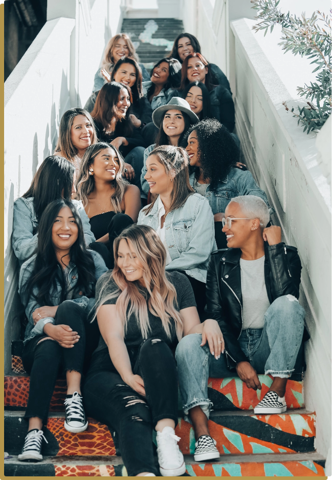 Group of women of all races and styles sitting on outdoor steps wearing different combinations of leather, jean, and sneakers